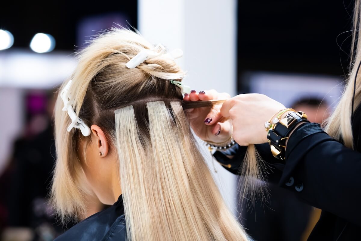 woman in salon getting hair extensions sewn into thinning hair